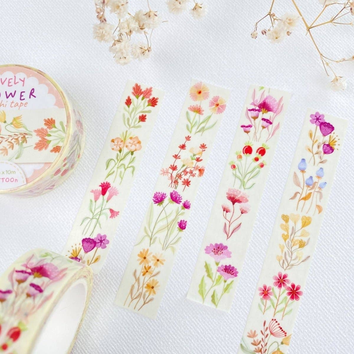 Floral washi tape rolls and strips displayed on a white textured fabric background, featuring delicate watercolor-style flowers in pink, red, orange, yellow, purple, and green.