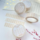 Three rolls of washi tape with a white and brown grid pattern are arranged on a textured white surface alongside matching strips and decorative gold foil paper. The labels on the rolls read 'WHITE & BROWN GRID washi tape' and show the brand 'Lettoo'.