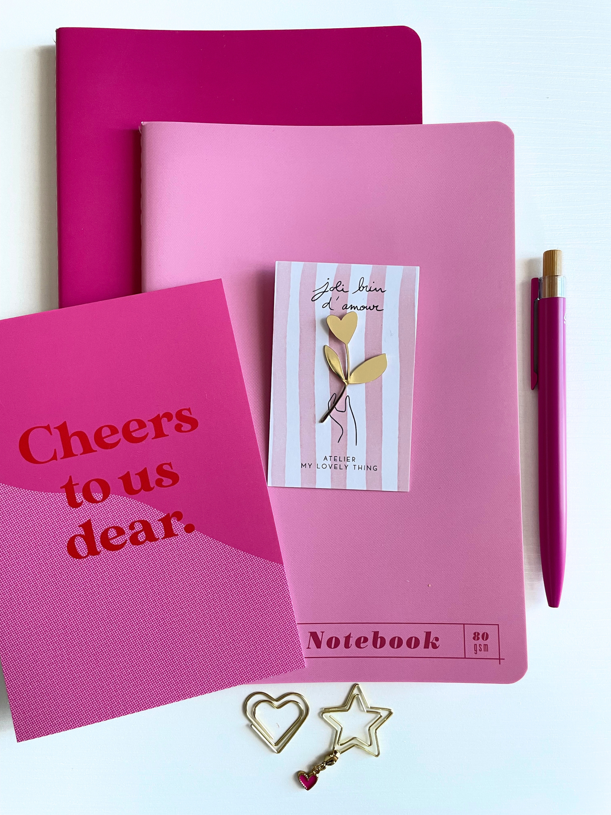 Pink notebook, card, and pen with decorative items on a white background