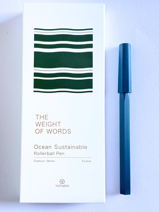 A YSTUDIO Ocean Sustainable Rollerball Pen in a deep blue color, shown next to its white packaging box which features dark green striped accents and gold text.