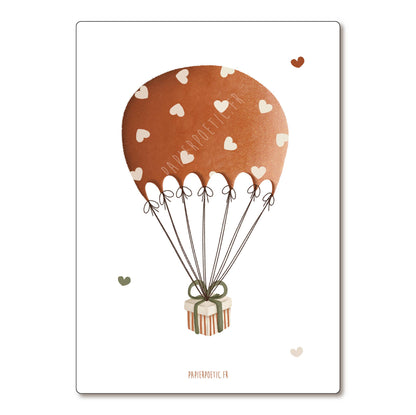 A minimalist art print featuring a brown watercolor hot air balloon with white heart patterns and a striped gift box, shown on a white background with a subtle drop shadow.