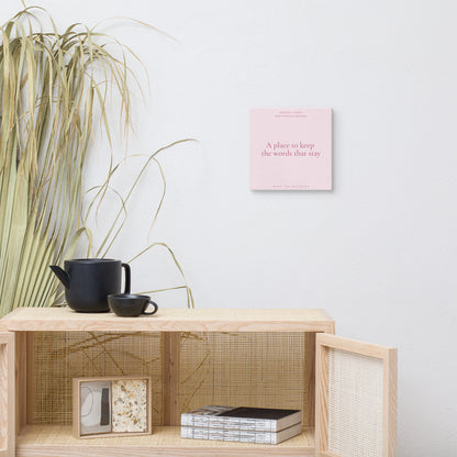 Wooden shelf with a teapot, cup, and books against a white wall with a pink book titled 'A place to keep the words that stay'.