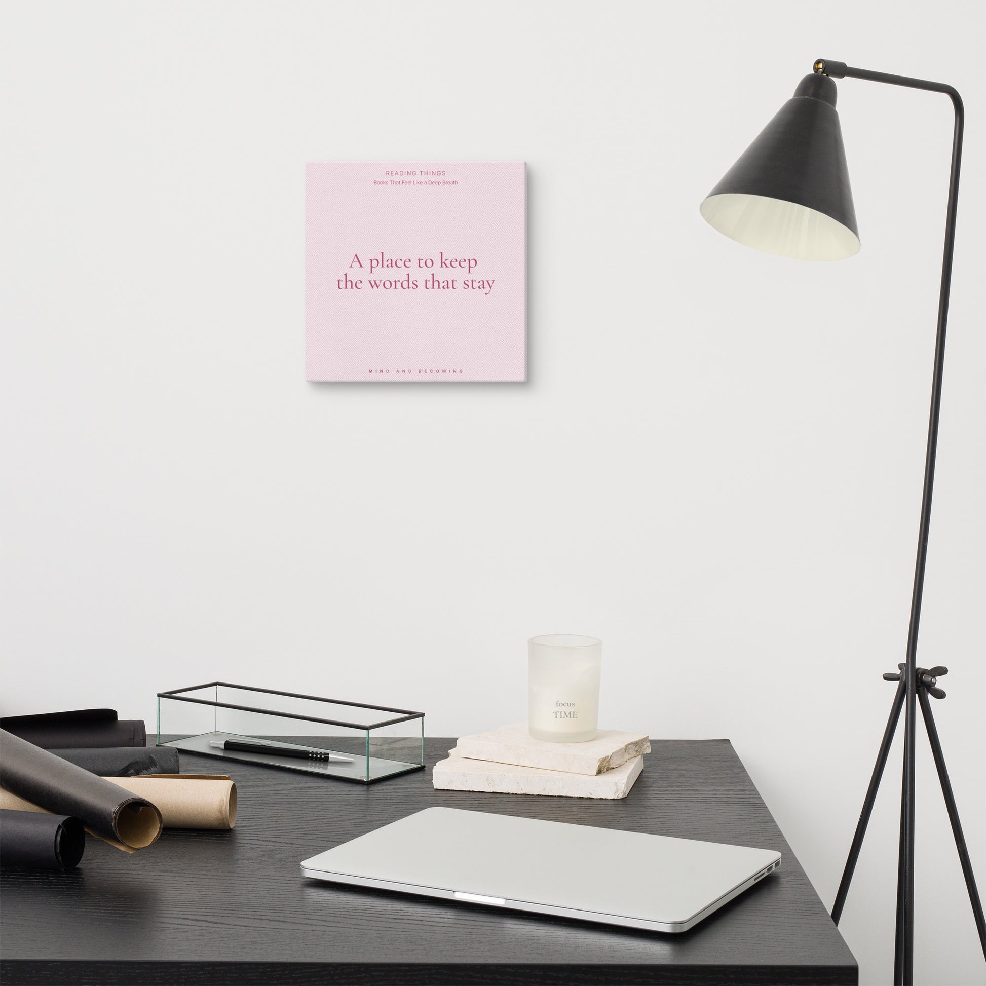 Minimalist desk setup with a pink book, lamp, and other items on a white wall background