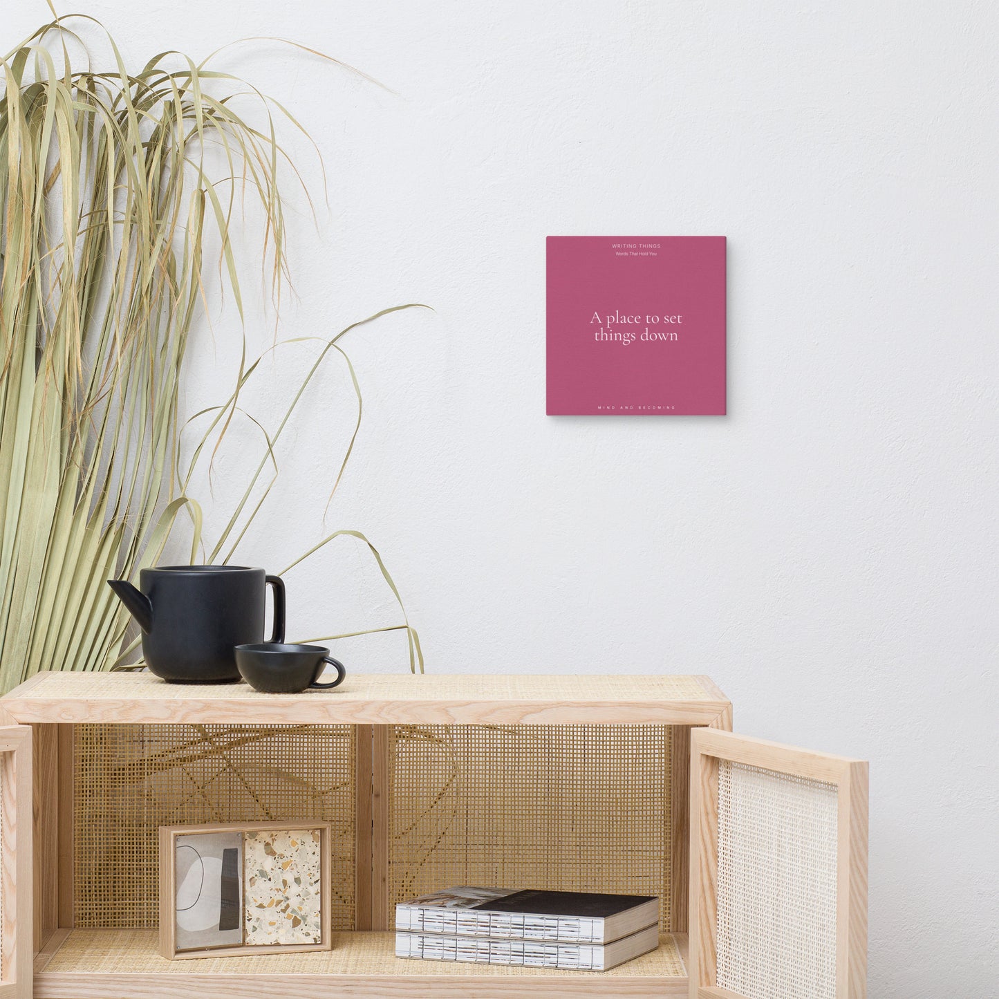 Wooden shelf with a teapot, cup, and decorative items against a white wall with a pink book.