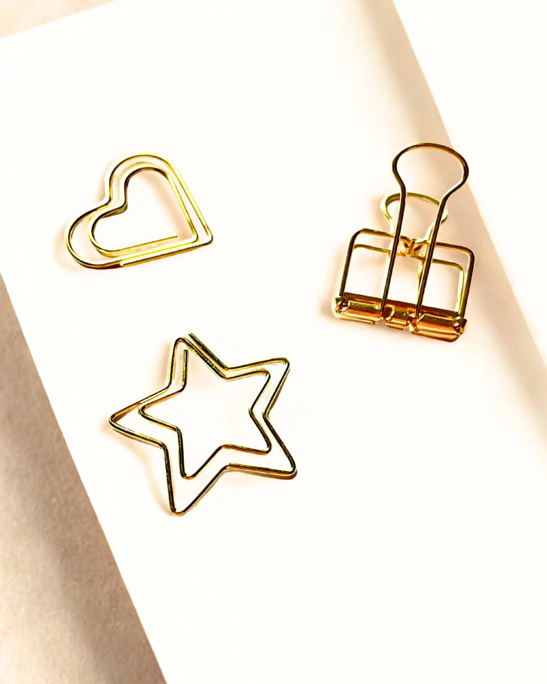 Three gold paper clips shaped like a heart, star, and square on a white background.