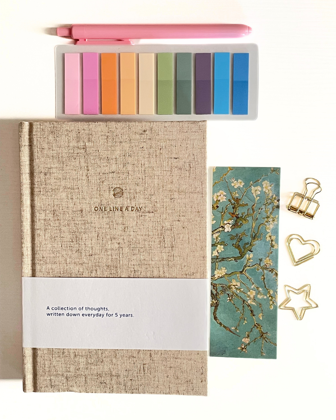 Journal with colorful bookmarks, a bookmark with floral design, and decorative clips on a light background.
