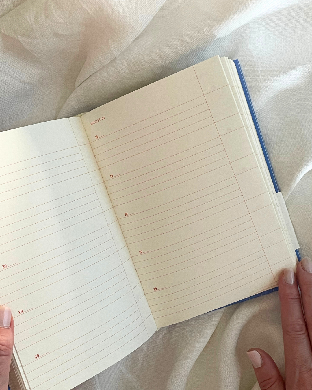 Open notebook with lined pages held by a person on a white fabric background