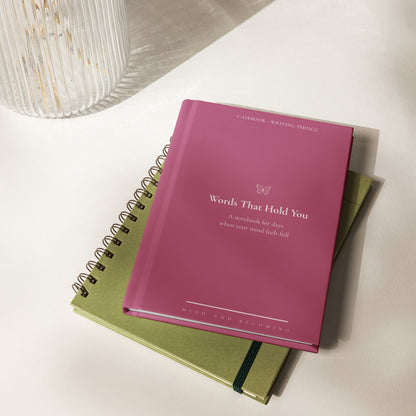 Pink notebook titled 'Words That Hold You' on a white surface