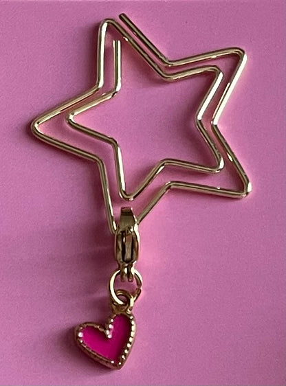 Gold star-shaped clip with a pink heart charm on a pink background
