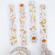 Four vertical strips of floral washi tape with a watercolor-style botanical pattern in muted orange, yellow, peach, and soft green on a white background. A roll of matching tape is partially visible at the bottom.