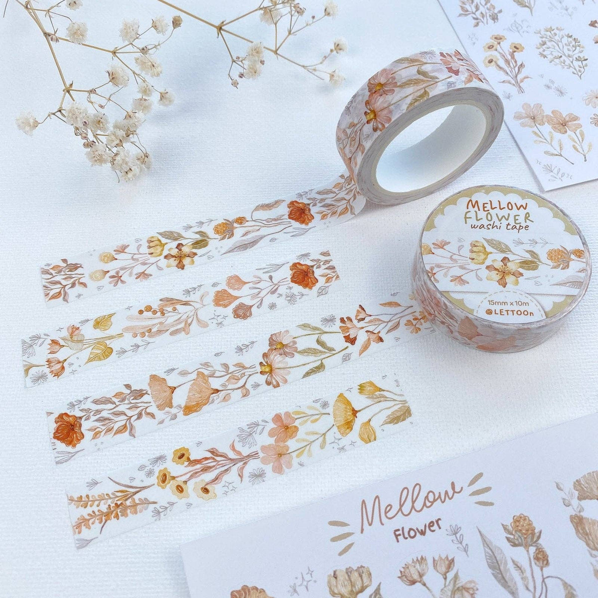 A roll of washi tape with a delicate floral pattern in muted orange, yellow, and brown tones, displayed alongside matching printed sheets on a white textured background.