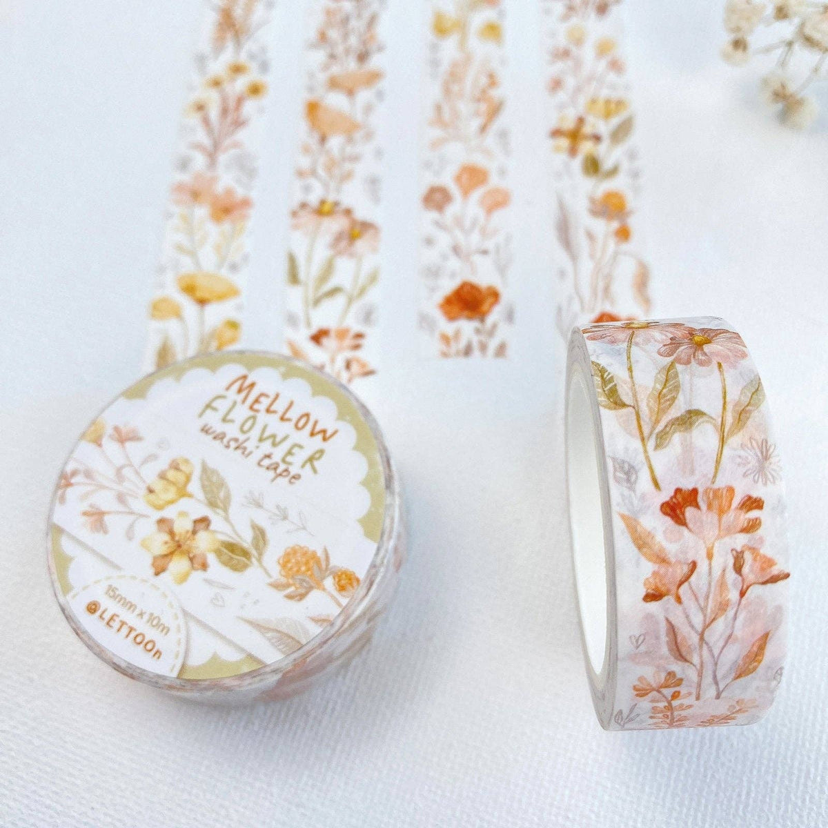 Two rolls of washi tape with a delicate floral pattern in soft orange, yellow, and green tones on a white background. One roll is sealed in clear plastic with a label reading 'Mellow Flower washi tape' and 'LETOON', while the other is partially unwrapped to show the pattern.