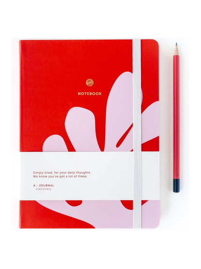 A red hardcover notebook with a white elastic closure band and abstract pink and white floral shapes on the cover, shown next to a red pencil on a white background.