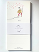 A vertical cream-colored notepad with a whimsical illustration of a girl in a glittery gold dress and red tights, holding a string that casts many red heart-shaped shadows. The notepad is wrapped in a white paper band printed with the brand name 'ATELIER MY LOVELY THING' and features lined writing space on the back.