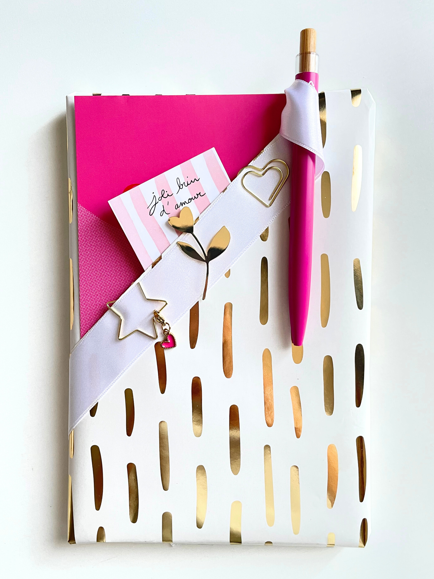 Notebook with gold accents, pink pen, and decorative items on a white background