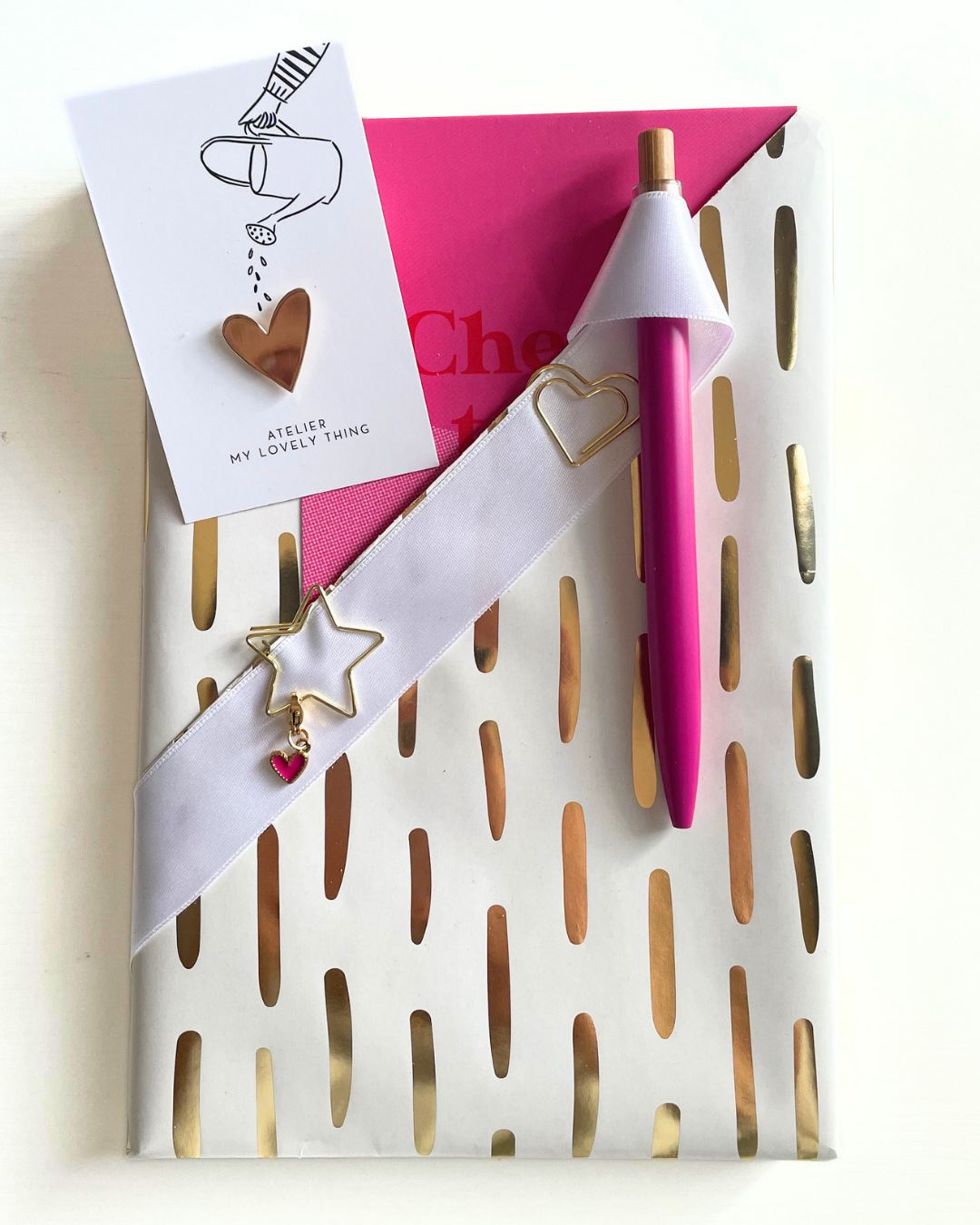 Decorative stationery set with pink pen, card, and gold heart-shaped clips on a white background