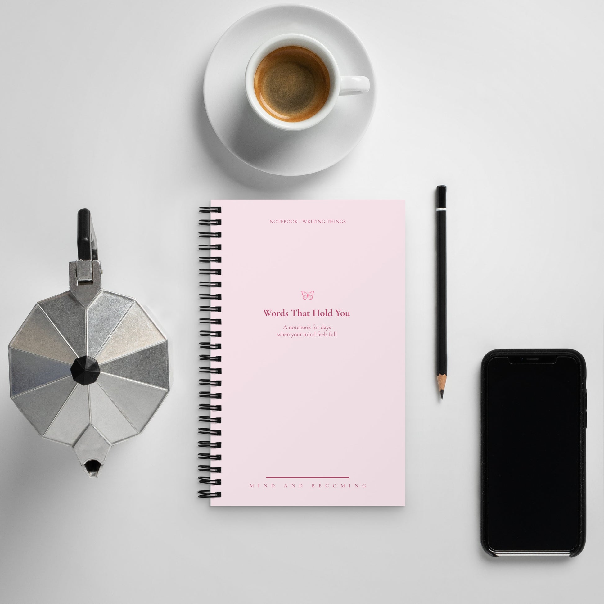 Notebook with a pink cover, coffee cup, phone, and other items on a light gray background