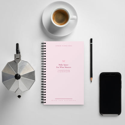 Notebook with a pink cover, coffee cup, phone, and coffee press on a light gray background