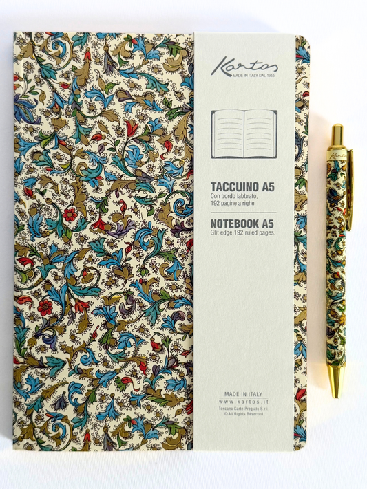 A Kartos Taccuino A5 notebook with an ornate multicolor floral patterned cover, shown next to a matching patterned pen on a white background.
