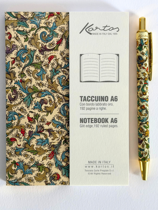 A Kartos A6 notebook with an ornate multicolor floral pattern on a beige cover, shown next to its cream-colored product box and a matching gold and patterned pen on a white background.