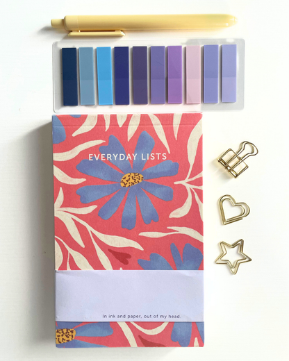 Notebook with floral design and 'Everyday Lists' text, surrounded by decorative clips on a light background.