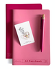 A pink A5 notebook with a matching pink pen and a small white card featuring a gold heart illustration, arranged on a white background.